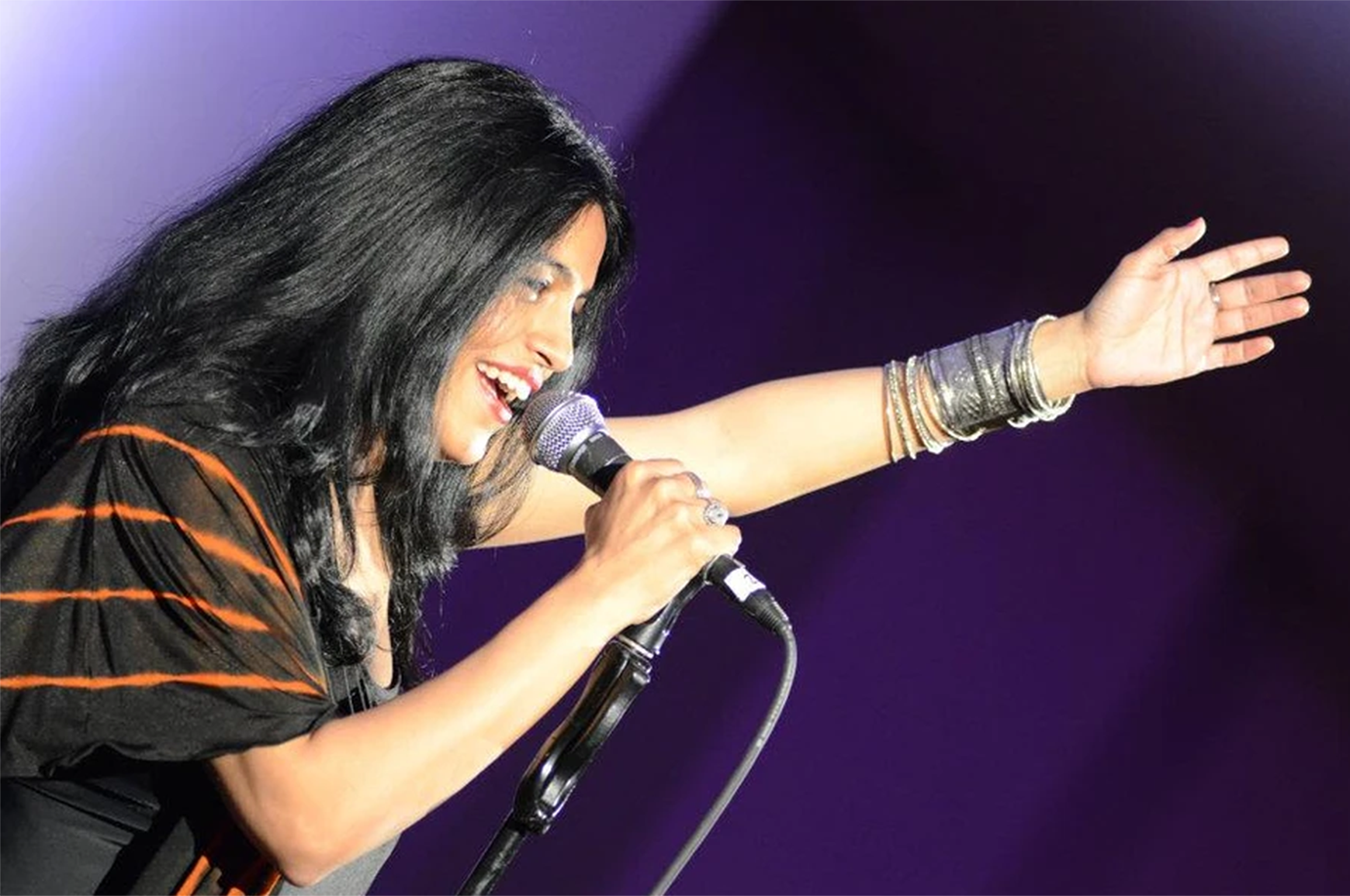 Image of singer Falu holding microphone singing with purple background